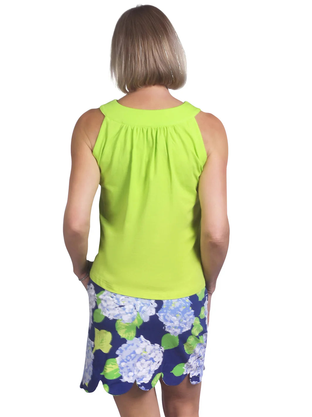 Person wearing a bright green sleeveless top and a blue floral skirt on a white background